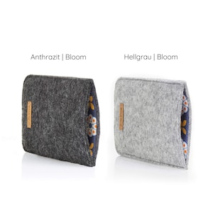 May include: Two felt pouches with a floral pattern on the back. The pouch on the left is dark gray and says "Anthrazit | Bloom". The pouch on the right is light gray and says "Hellgrau | Bloom".