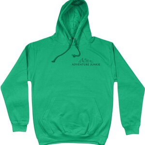 May include: A bright green hoodie with a drawstring hood and a kangaroo pocket. The hoodie features a black graphic of mountains and the text "ADVENTURE JUNKIE" printed on the chest. The sweatshirt is made of a soft material.