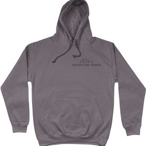 May include: A gray hooded sweatshirt with a front pocket and drawstring. The text "ADVENTURE JUNKIE" is printed below a mountain graphic on the chest. The hoodie is made of a soft material.