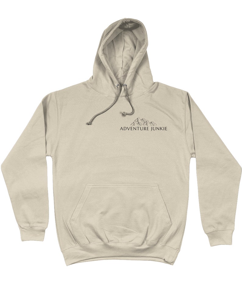 May include: A tan hoodie with a drawstring hood and a front pocket. The hoodie features a small mountain graphic and the text "ADVENTURE JUNKIE" printed in black. The hoodie is made of a soft material.