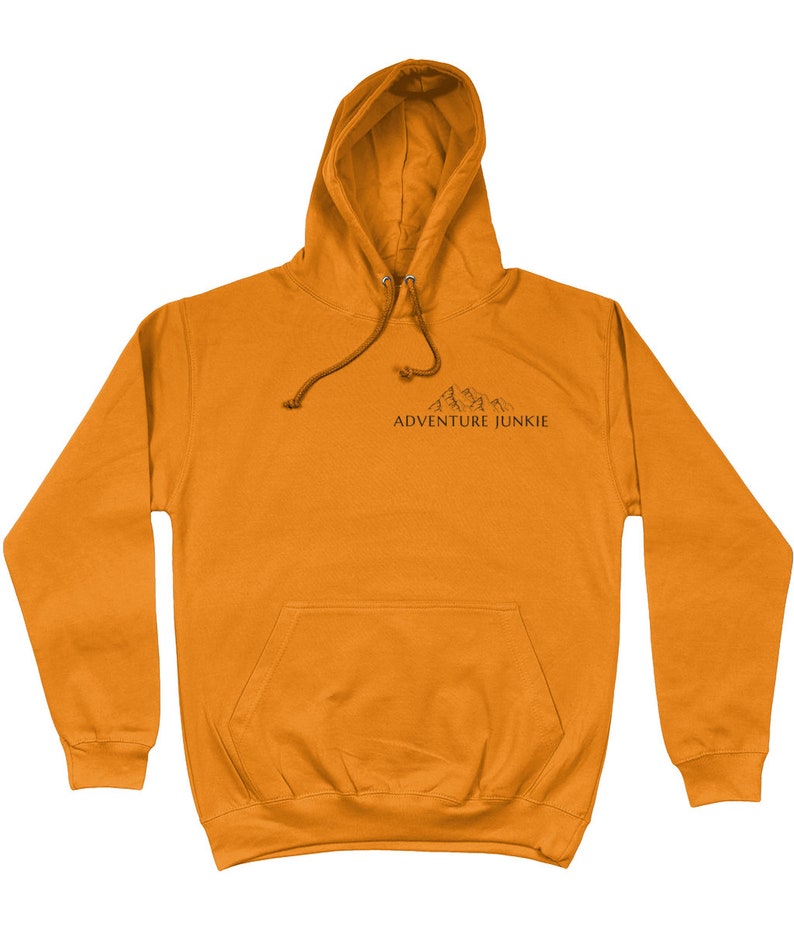 May include: Mustard-colored hoodie with a drawstring hood and a front pocket. The hoodie features a small mountain graphic and the text "ADVENTURE JUNKIE" printed in black. A casual, comfortable garment for outdoor enthusiasts.