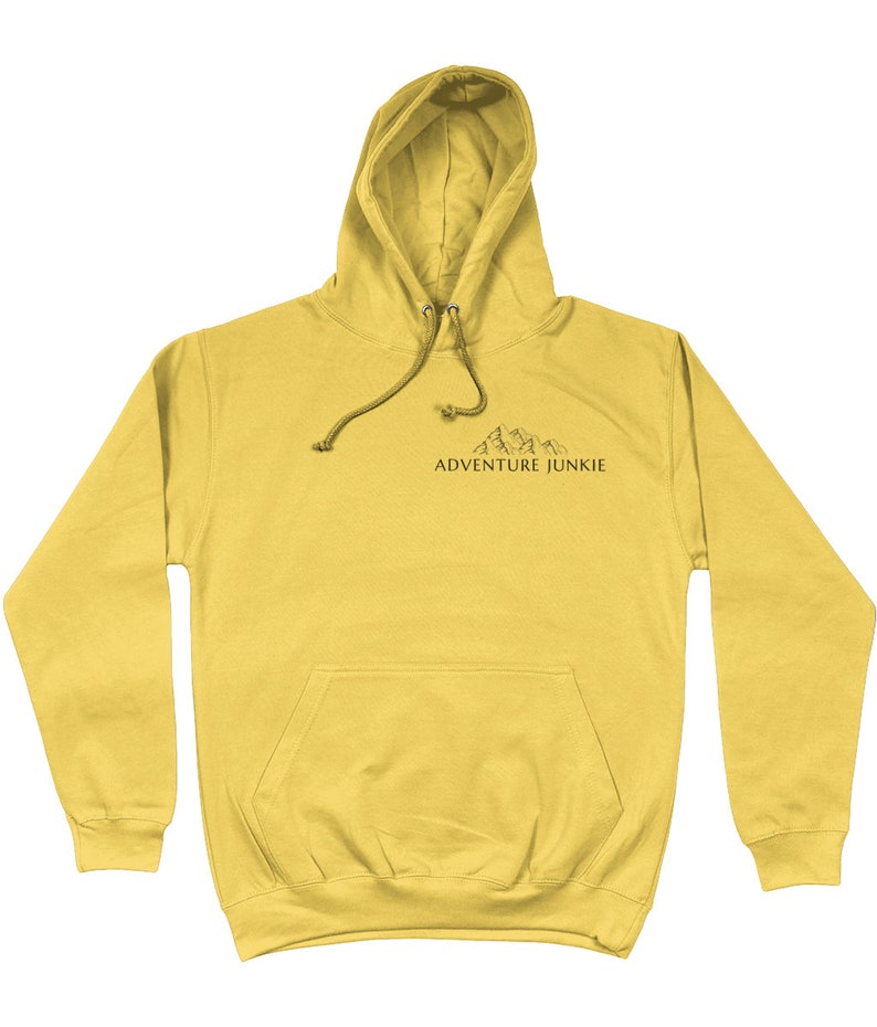 May include: Mustard yellow hoodie with a drawstring hood and a front pocket. The hoodie features a small mountain graphic and the text "ADVENTURE JUNKIE" printed in black.