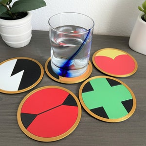 May include: Five round coasters with different colored and patterned designs. The coasters have a gold trim and are arranged on a wooden surface.