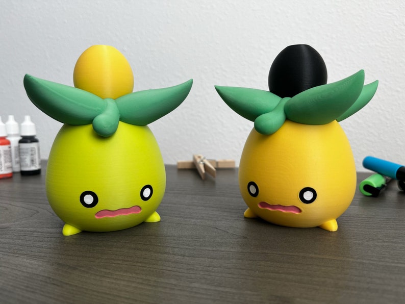 May include: Two small, hand-painted figurines of cartoon characters. The figurines are yellow and green with black eyes and pink mouths. One figurine has a black top hat and the other has a yellow top hat.