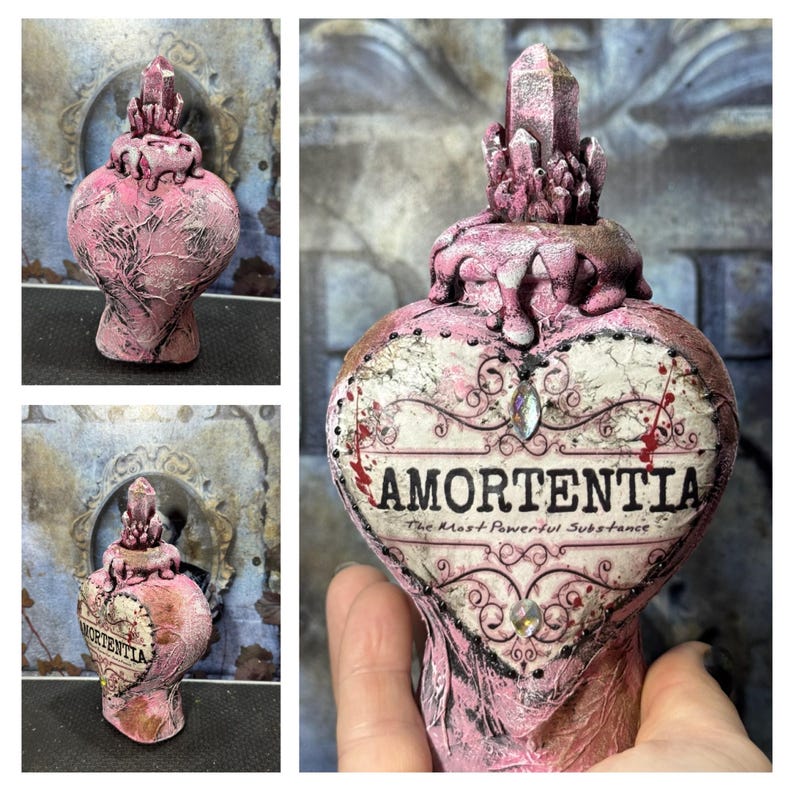 Puede incluir: Una botella de poci&oacute;n Amortentia rosa en forma de coraz&oacute;n con un tap&oacute;n de cristal. La botella tiene una superficie texturizada y las palabras "Amortentia, The Most Powerful Substance" est&aacute;n impresas en la parte delantera. Tambi&eacute;n hay cristales y adornos decorativos.