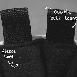 May include: Close-up of the inside of a black bag with a fleece lining. The bag has two black double belt loops at the top.