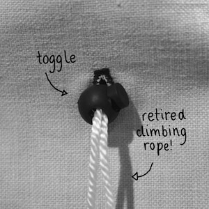 May include: A black toggle with a white rope attached to it. The rope is labeled "retired climbing rope!" and the toggle is labeled "toggle".