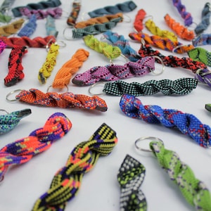 May include: A collection of numerous twisted paracord keychains in a wide variety of vibrant colors and patterns, including neon orange, lime green, blue, purple, and black, each featuring a circular metal split ring for attachment.