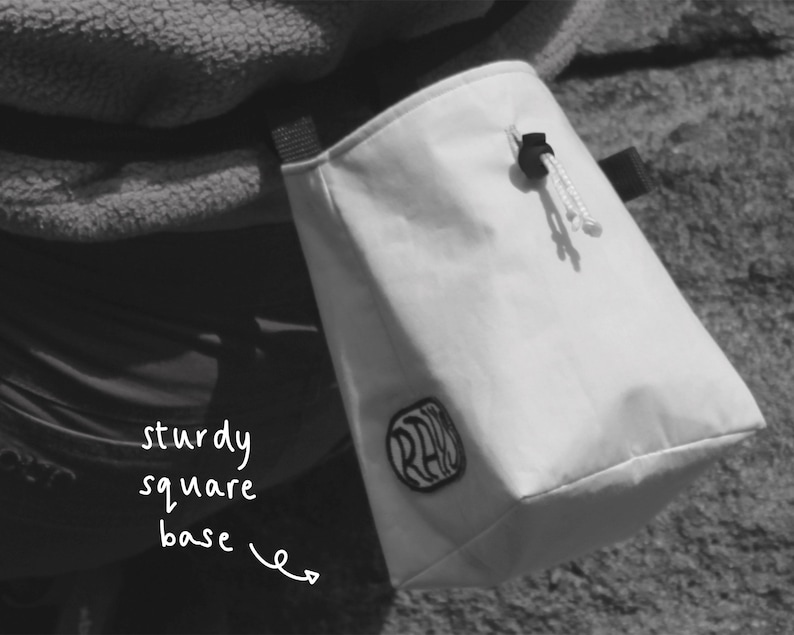 May include: White chalk bag with a black logo that says "RAD" and a sturdy square base. The bag is hanging from a person's belt.