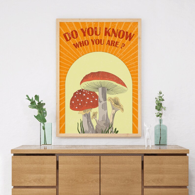 May include: A framed art print featuring a whimsical illustration of mushrooms in shades of red, white, and gray against a yellow backdrop. The text "DO YOU KNOW WHO YOU ARE?" is displayed in orange. The artwork is in a wooden frame.
