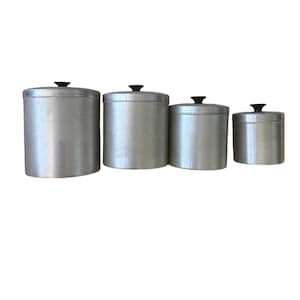 May include: Set of four aluminum canisters with black knob lids. The canisters are cylindrical and vary in size, perfect for kitchen storage. The metal has a brushed finish, giving them a vintage look. Ideal for storing dry goods.