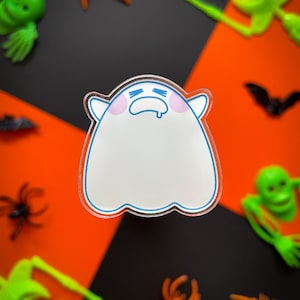 May include: A white ghost with a blue outline and pink cheeks is crying. The ghost is on a black and orange background with green and orange Halloween decorations.