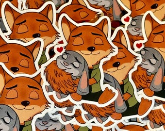 May include: A stack of stickers featuring a cartoon fox and rabbit hugging. The fox is orange and the rabbit is gray. The stickers have a white border and a red heart on each.