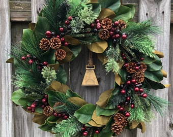 Magnolia Christmas wreath with pine, gold bell, berries,and pinecones. 24” southern charm magnolia perfect for home decor, gifts and events.