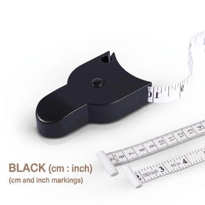 Puede incluir: Una cinta métrica corporal retráctil de color negro con una cinta blanca que presenta marcas tanto en centímetros como en pulgadas. La cinta se extiende desde la carcasa de plástico negro, que incluye un botón central y una ranura.