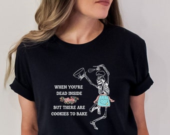 May include: Black t-shirt featuring a skeleton chef with a mixing bowl and whisk, wearing an apron. The shirt includes the text: "When you're dead inside but there are cookies to bake."