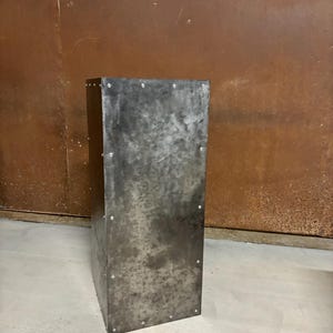 May include: A tall, rectangular metal planter with a distressed, aged finish. The planter has a rustic, industrial look and is made of thick metal.