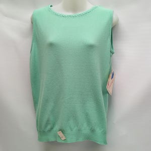 May include: A sleeveless, mint green sweater top. The top has a round neckline with a braided trim and a ribbed hem. A tag is attached to the bottom of the sweater. The sweater is displayed on a mannequin.