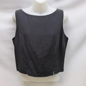 May include: Black sleeveless top with a white polka dot pattern. The top has a scoop neckline and a straight hemline with a small slit at the bottom. The garment is displayed on a white mannequin.