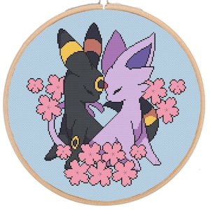 Può includere: Motivo a punto croce ricamato con due personaggi Pokémon, un Umbreon nero e giallo e un Espeon viola, con fiori di ciliegio rosa intorno.