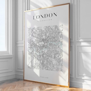 May include: A framed print of a map of London, with the city's name at the top and 'England' at the bottom. The map is in black and white, with a gold frame. The print is displayed on a white wall, with a wooden floor.