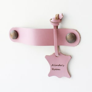 May include: A pink leather door handle with a brass knob and a pink leather tag that says "Alinda's Room".