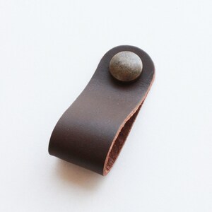 Könnte beinhalten: Ein brauner Leder-Schubladenzug mit einem Metallknopf.