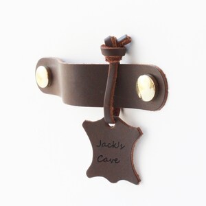 Könnte beinhalten: Brauner Leder-Türgriff mit einem Messingknopf und einem Lederanhänger mit der Aufschrift "Jack's Cave".