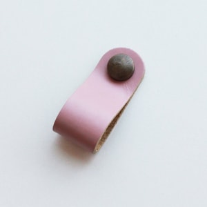 Könnte beinhalten: Ein rosa Ledergriff mit einem Metallknopf. Der Griff ist für die Verwendung an einer Schublade oder einem Schrank konzipiert.