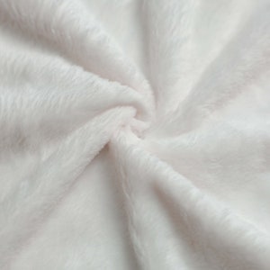 May include: Close-up of a soft, white, fluffy fabric with a smooth texture. The fabric is folded and draped, creating a gentle, flowing pattern.
