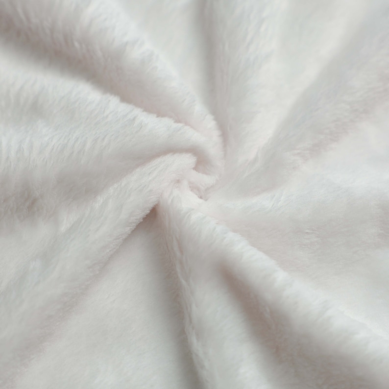 May include: Close-up of a soft, white, fluffy fabric with a smooth texture. The fabric is folded and draped, creating a gentle, flowing pattern.