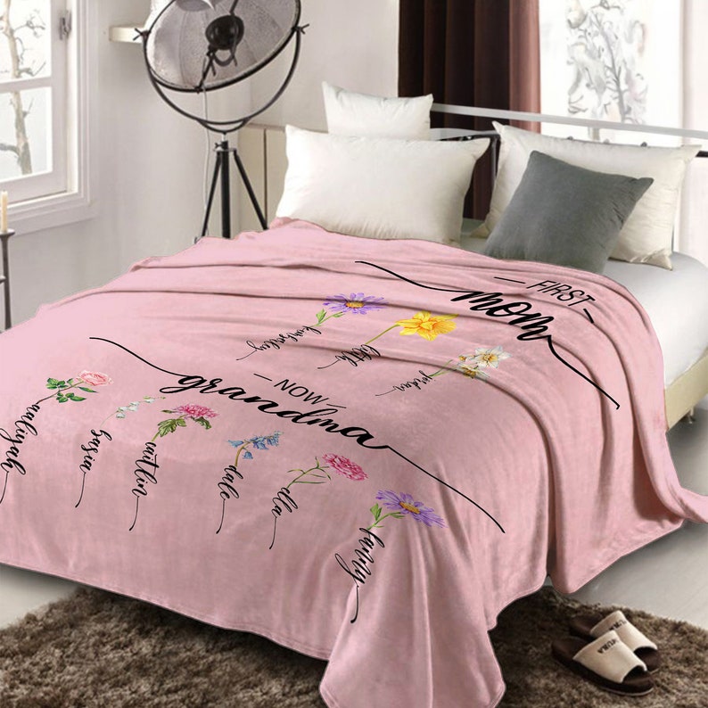 K&ouml;nnte beinhalten: Rosafarbene Fleece-Decke mit Blumenmuster und dem Text "First Mom - Now Grandma".