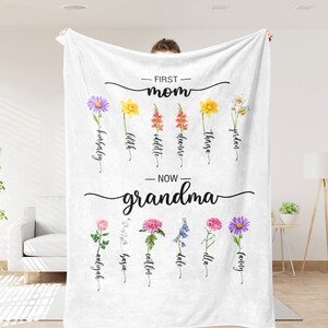 K&ouml;nnte beinhalten: Eine wei&szlig;e Fleece-Decke mit dem Text "FIRST - mom" und "NOW - grandma" darauf gedruckt. Die Decke zeigt ein Blumenmuster mit den Namen der Kinder und Enkelkinder unter jeder Blume.