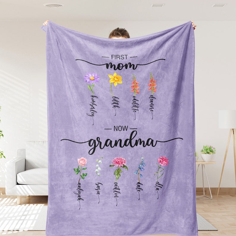 K&ouml;nnte beinhalten: Eine lilafarbene Fleece-Decke mit dem Text "First Mom Now Grandma" und floralen Illustrationen. Die Blumen sind mit Namen wie "kinsley", "little", "addison", "eliana", "madilyn", "joya", "caitlyn", "dale" und "ella" beschriftet.