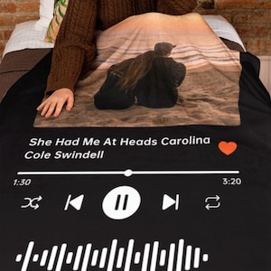 Op de afbeelding: Zwart-witte Spotify-achtige deken met een stel dat op een strand zit. De titel van het nummer is "She Had Me At Heads Carolina" van Cole Swindell. Het nummer is gepauzeerd op 1:30.