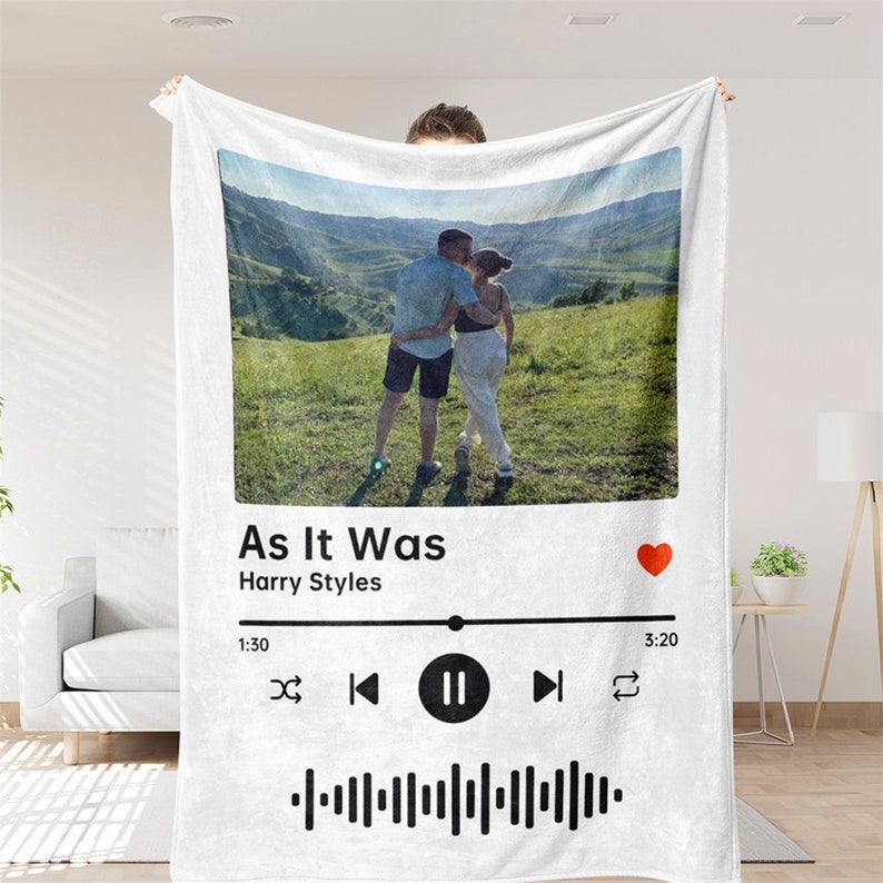Op de afbeelding: Witte fleece deken met een foto van een stel in een veld, een Spotify-achtige muziekspeler-afbeelding met het nummer "As It Was" van Harry Styles en een rood hartpictogram.