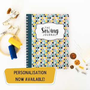 May include: A blue and yellow patterned journal with the text "The Sewing Journal" on the cover. The journal has a spiral binding and is surrounded by sewing supplies, including thread, needles, and a measuring tape.