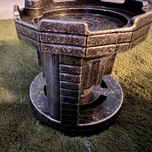 May include: A silver metal tower with a round top and a base with a circular design. The tower has a textured surface and appears to be made of metal.