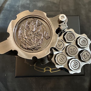 May include: A white ceramic mug with a black handle and the text "But First, Coffee" in a bold, black font. The mug is set against a blurred background, suggesting a cozy setting.