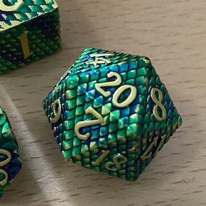 May include: A green and blue dice with gold numbers. The dice has a snake skin pattern.
