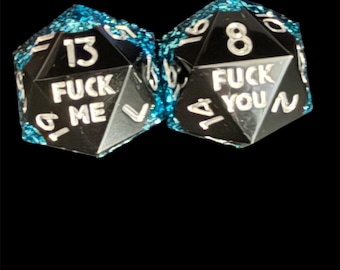 Peut inclure: Deux dés noirs à plusieurs faces avec des chiffres et du texte blancs. L'un des dés indique "13 FUCK ME" et l'autre "8 FUCK YOU". Les bords sont ornés d'un matériau bleu clair étincelant.