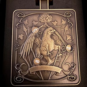 May include: Bronze pendant with a detailed relief design. The pendant features a griffin, a tree, stars, and dice. The top has a small loop for a chain. The design is framed by ornate scrollwork. The dice show the numbers 2, 4, 7, 8, and 9.
