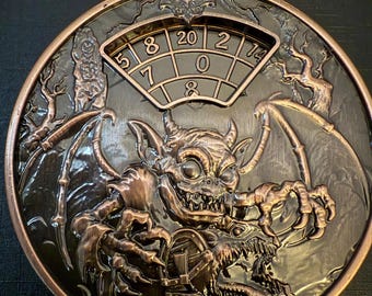 May include: A bronze-colored, circular decorative piece with a devilish gargoyle design. The piece features a dial with numbers and the text "20 10 D8" at the top. The gargoyle has bat wings and is holding a chest.