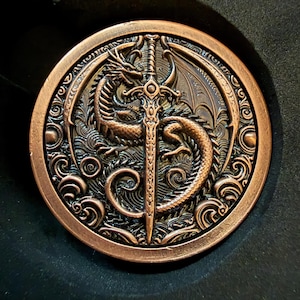 May include: A circular copper-toned metal coin featuring a detailed relief of a dragon coiled around a central sword. The background displays intricate swirling wave patterns, and the outer border is decorated with a series of small circular motifs.