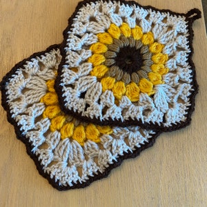 May include: Two crocheted pot holders in the shape of sunflowers. The pot holders are brown, beige, and yellow.