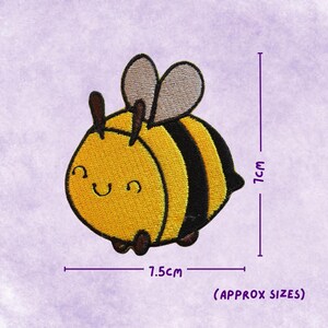 May include: Embroidered bee patch with a smiling face, yellow and black stripes, brown antennae, and grey wings. The patch is approximately 7.5cm wide and 7cm tall. The text "(APPROX SIZES)" is below the dimensions.