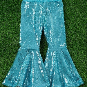 May include: Teal blue sequined bell bottom pants. The pants have a wide leg opening and are made of a sparkly fabric.