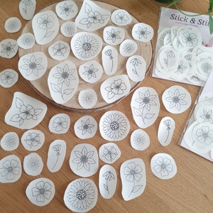 Könnte beinhalten: Eine Sammlung weißer Stoffkreise mit schwarzen Stickereien verschiedener Blumen. Die Kreise sind auf einer Holzoberfläche angeordnet und ein Blatt weißer Stoffkreise mit schwarzen Stickereien befindet sich im Hintergrund. Der Text "Stick & Stix Embroidery Designs" ist auf dem Blatt Stoffkreise sichtbar.
