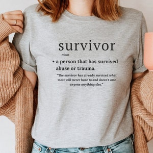 May include: A grey t-shirt with the word "survivor" printed on it in black text. The word "survivor" is defined as "a person that has survived abuse or trauma." The quote "The survivor has already survived what most will never have to and doesn't owe anyone anything else." is printed below the definition.
