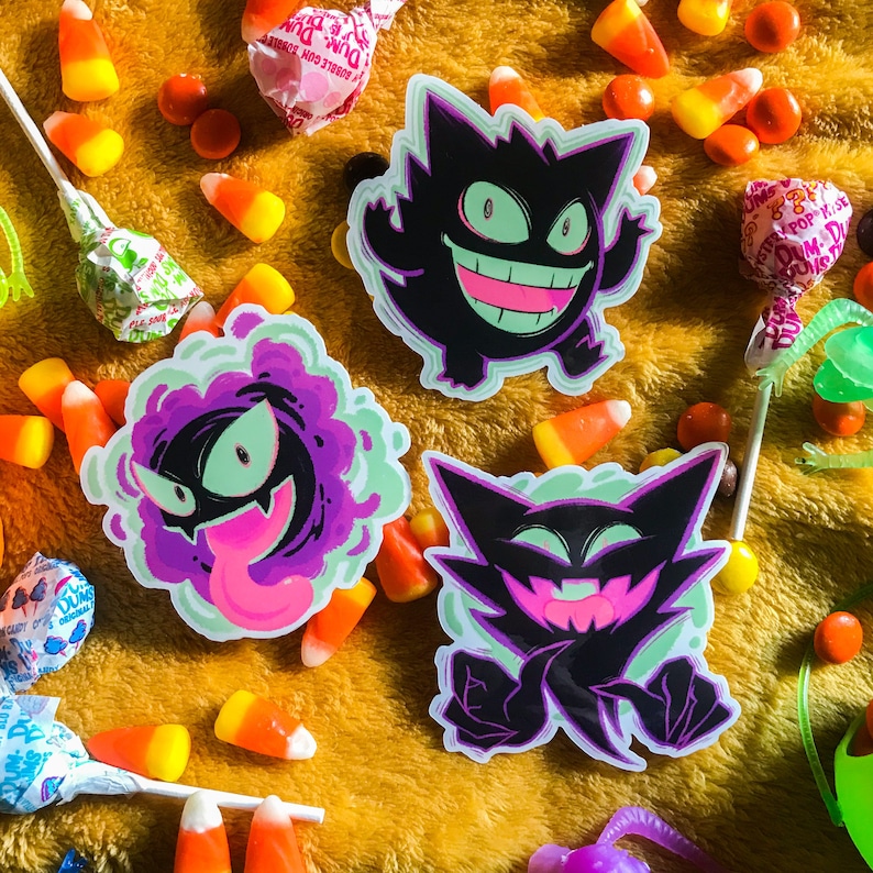 Pu&ograve; includere: Tre adesivi Pokemon di tipo Spettro con Gengar, Haunter e un Gengar con un'aura viola. Gli adesivi sono su una superficie gialla pelosa con mais dolce e lecca-lecca.